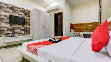 A hotel room with a bed, a TV mounted on the wall, a wardrobe, and a small kitchenette area.