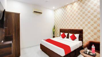 A hotel room with a bed, a TV, a ceiling fan, a patterned wall, and a small table with a bottle and glasses.