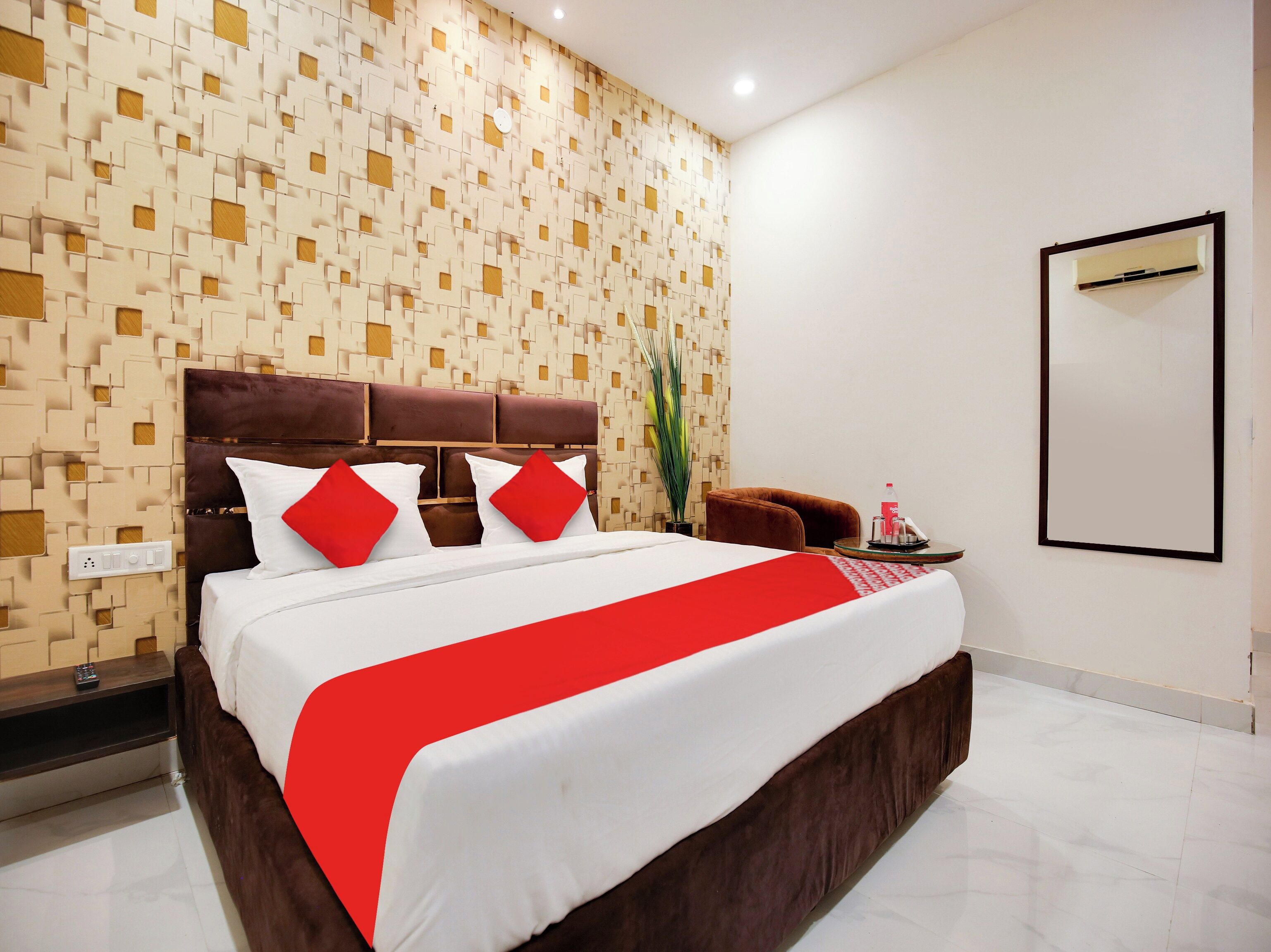 Une chambre d’hôtel au design moderne, dotée d’un grand lit agrémenté d’une touche de rouge, d’une tête de lit marron et d’un mur orné de motifs.