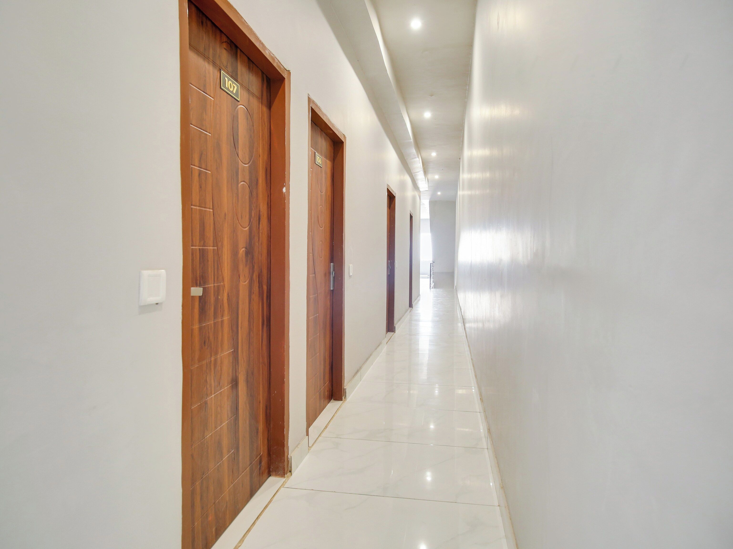 A corridor with wooden doors, white walls, and a tiled floor.