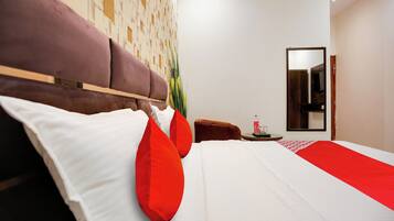 A modern hotel room with a large bed, a wooden headboard, a small side table, and a mirror on the wall.