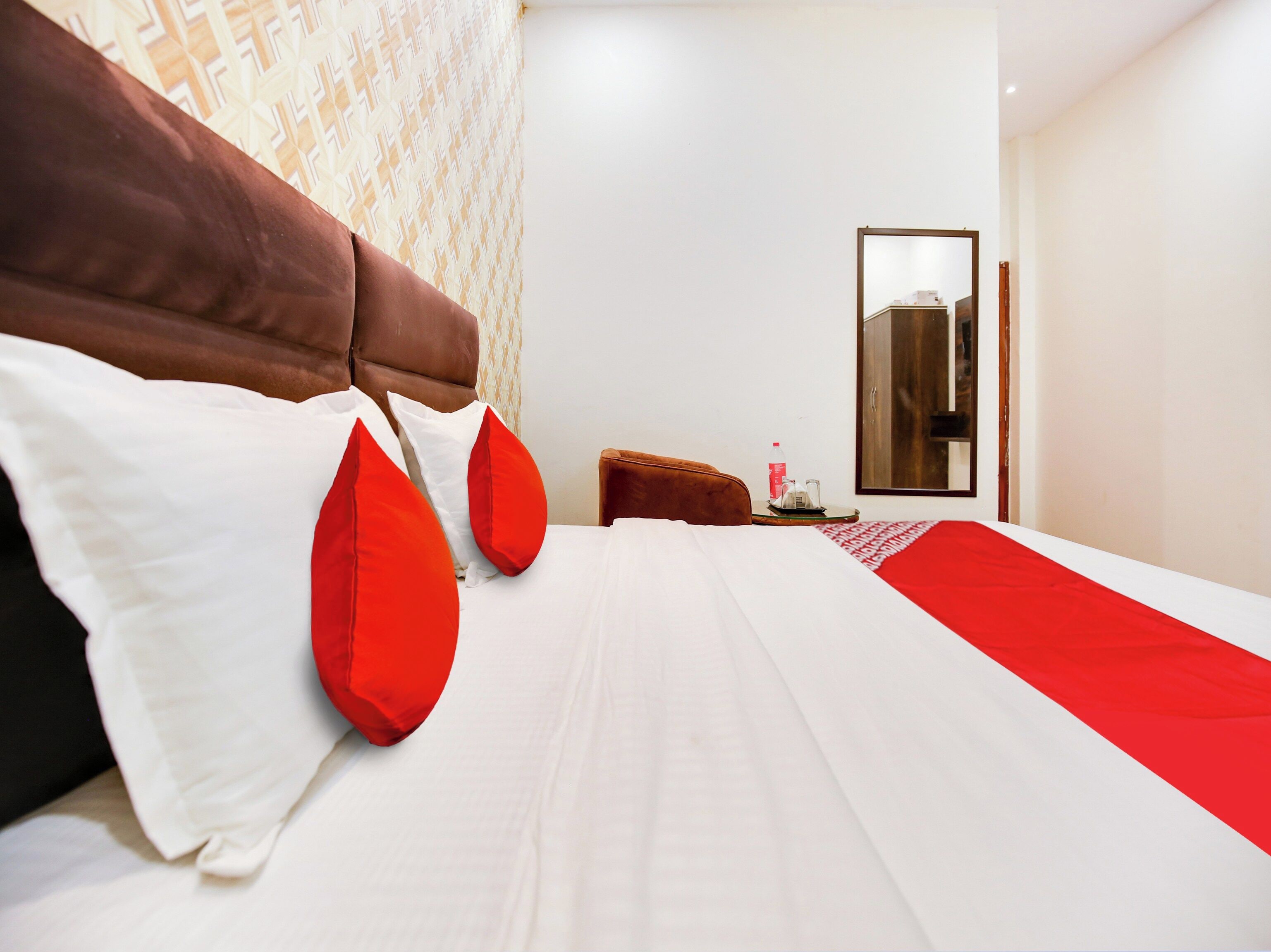 A hotel room with a bed, pillows, a side table, a mirror, and a wardrobe.