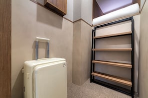 A compact room with a white suitcase, a wooden shelf unit, and a wall-mounted rack.