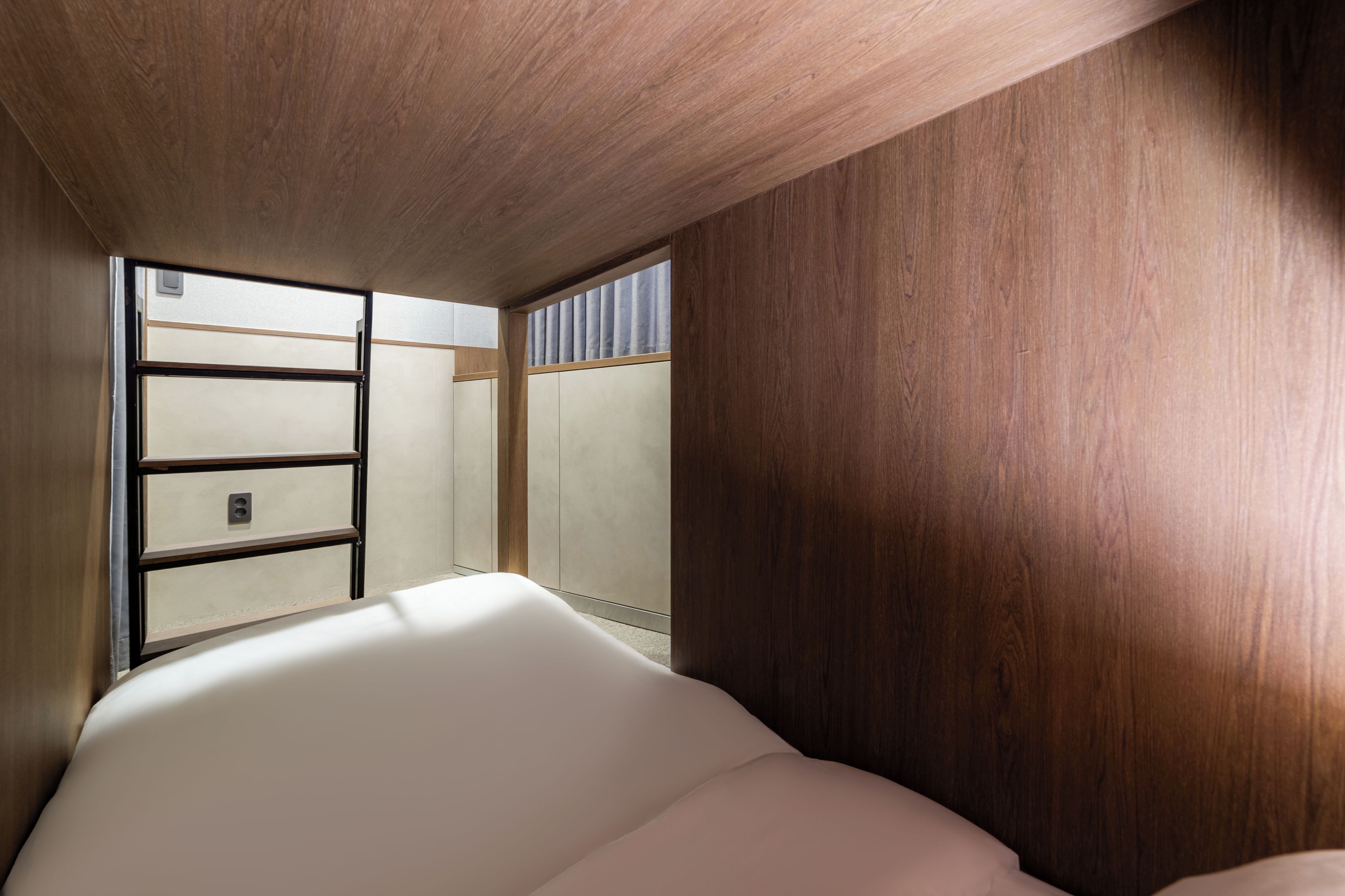 Quarto com teto de madeira, cama com roupa de cama branca e janela com persianas.