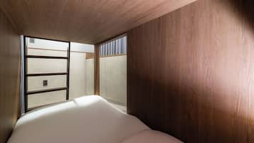 Quarto com teto de madeira, cama com roupa de cama branca e janela com persianas.