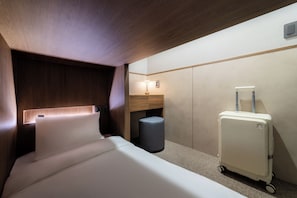 A hotel room with a bed, a desk, a lamp, and a suitcase.