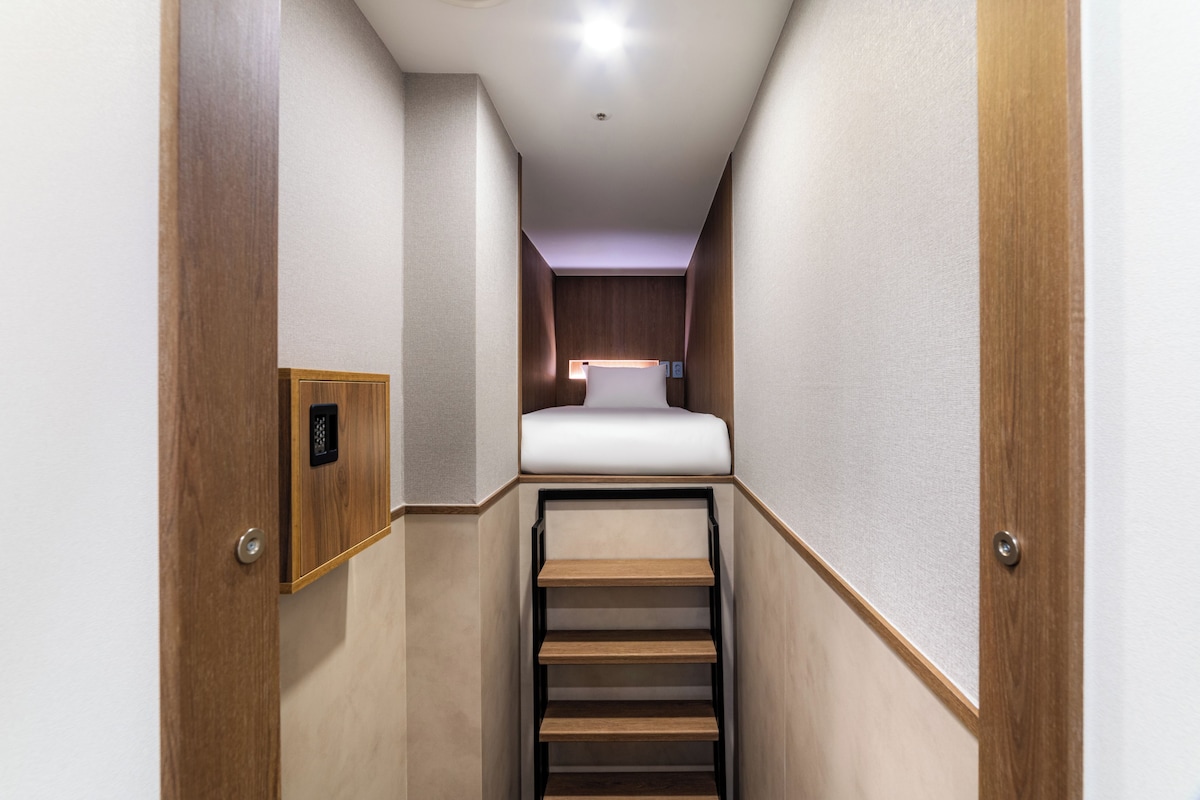 A narrow, enclosed space with a bed at the end, a small shelf, and a door with a lock.