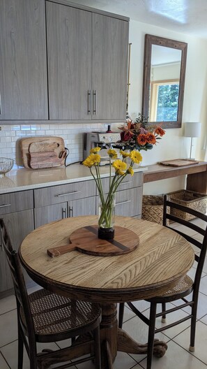 A kitchen with grey cabinets, a coffee machine, a vase with yellow flowers, and a round wooden table with chairs.