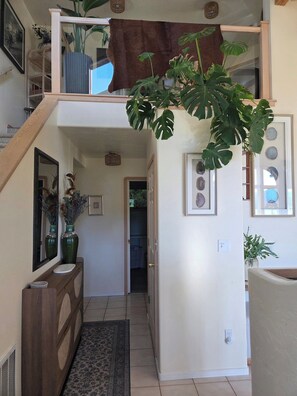 Ein mehrgeschossiges Interieur mit einer Treppe, einem zur Tür führenden Gang und einer großen Pflanze.