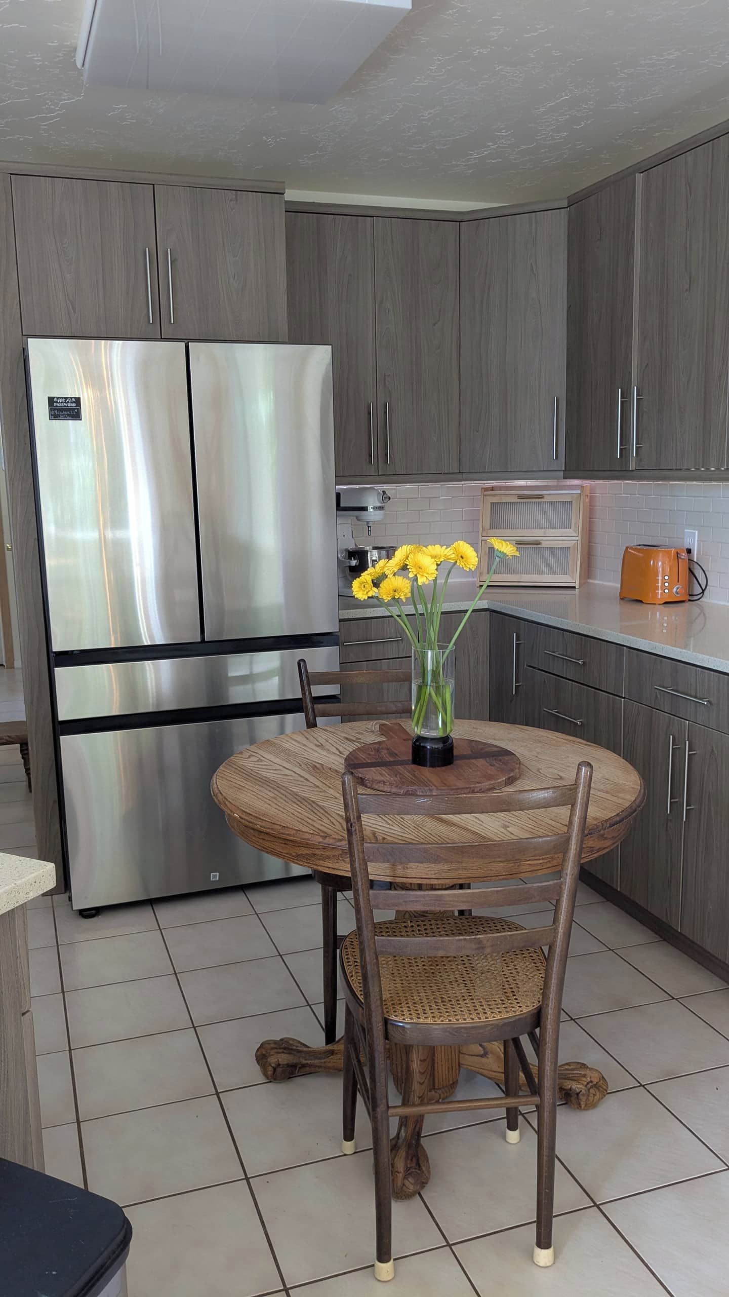 A modern kitchen with a built-in stainless steel refrigerator, a round wooden dining table with chairs, and a vase with yellow flowers.