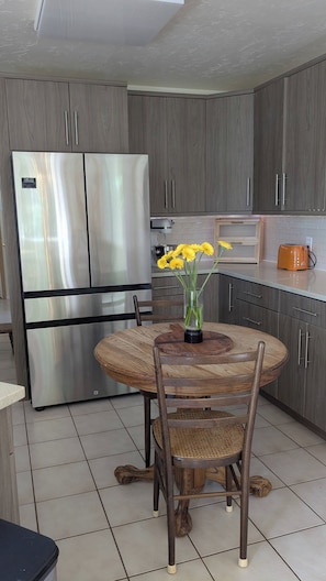 Eine moderne Küche mit einem eingebauten, edlen Kühlschrank aus Edelstahl, einem runden Holzesstisch mit Stühlen und einer Vase mit gelben Blumen.