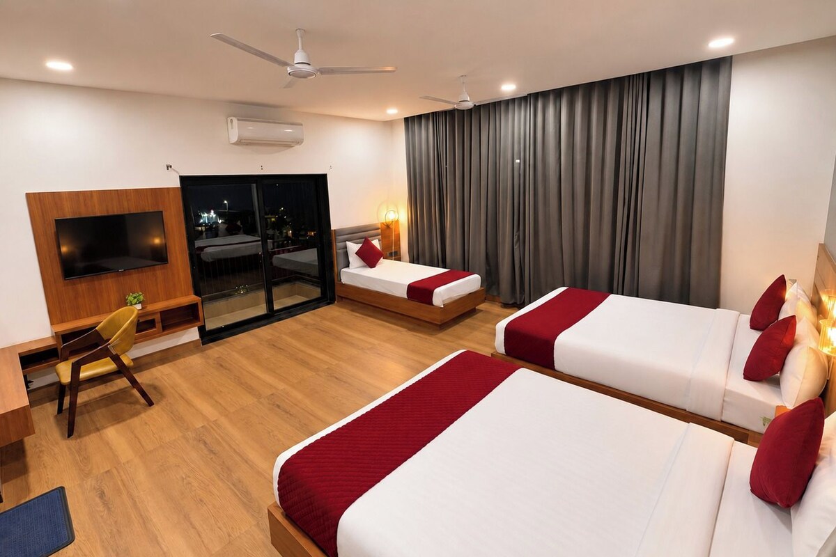 Ein Hotelzimmer mit zwei Betten, einem Fernseher, einem Schreibtisch und einem Balkon.