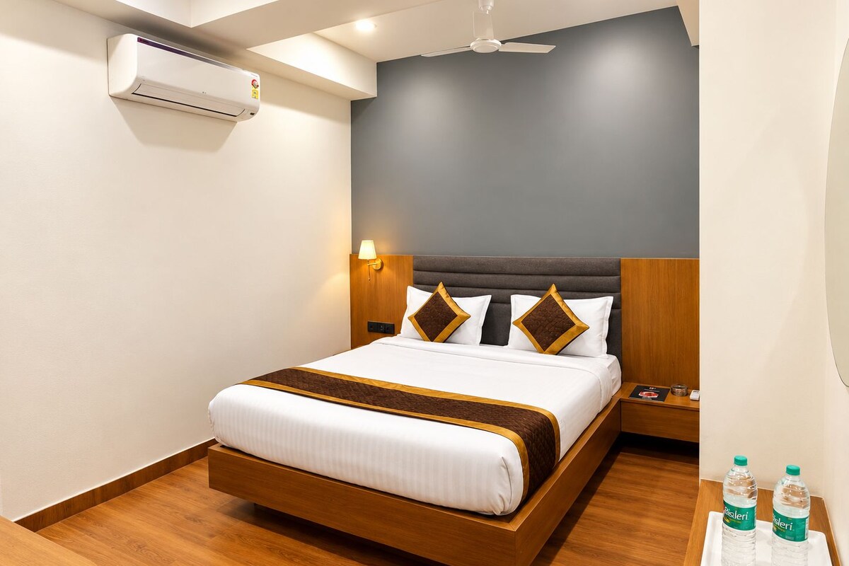 Ein Hotelzimmer mit Bett, Nachttischen, einer Klimaanlage, Deckenventilator und einem Beistelltisch mit Wasserflaschen.