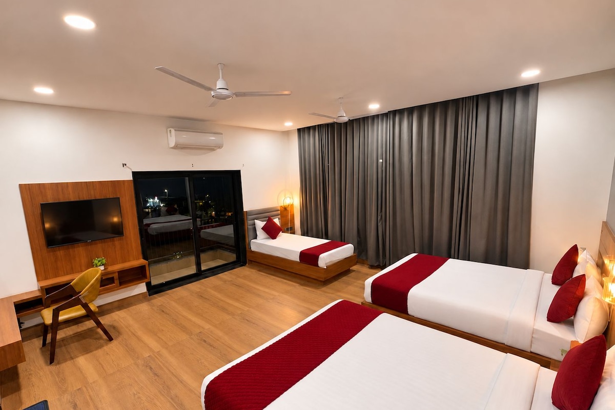 Ein Hotelzimmer mit zwei Betten, einem Fernseher, einem Schreibtisch und einem Balkon mit Blick auf die Stadt.