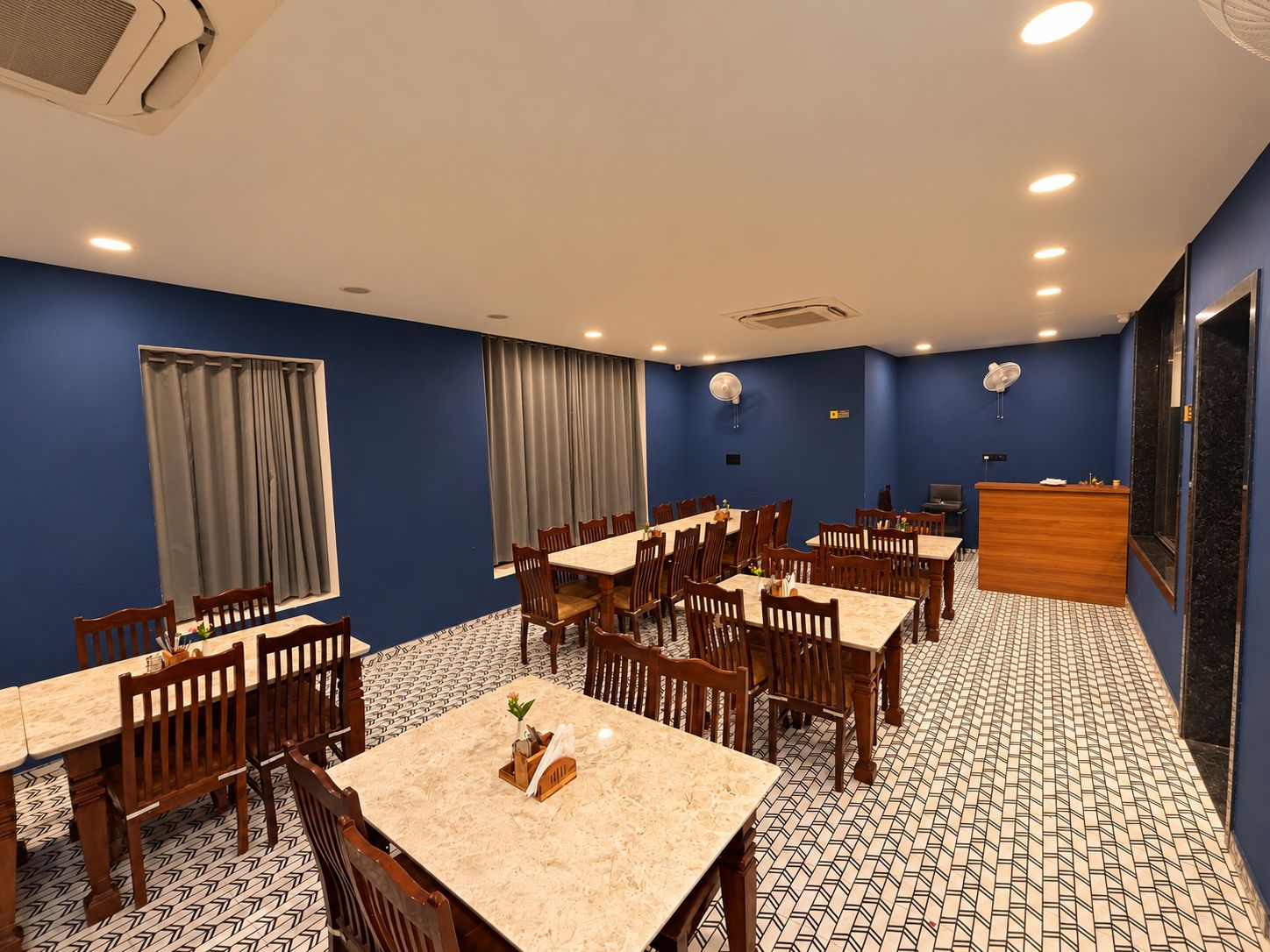 Ein Hotel-Essbereich mit mehreren Tischen und Stühlen, einer Rezeption und einem gemusterten Boden.