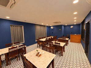 Ein Hotel-Essbereich mit mehreren Tischen und Stühlen, einer Rezeption und einem gemusterten Boden.