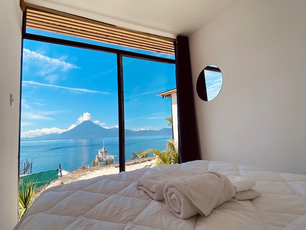 Un dormitorio con un ventanal que ofrece vistas a una playa y una montaña.