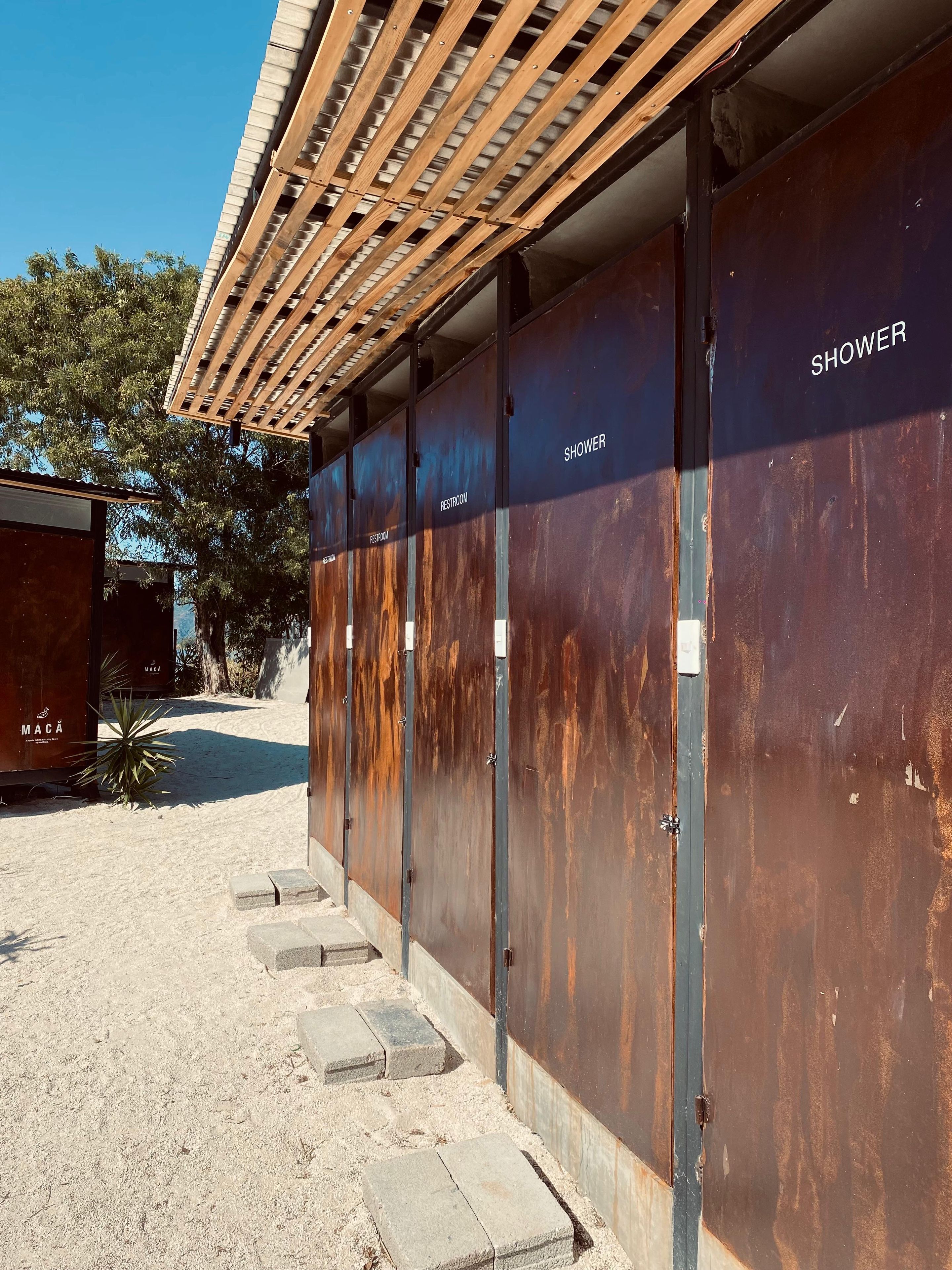 Fila de cabinas de ducha y baños de metal con una pérgola de madera encima.