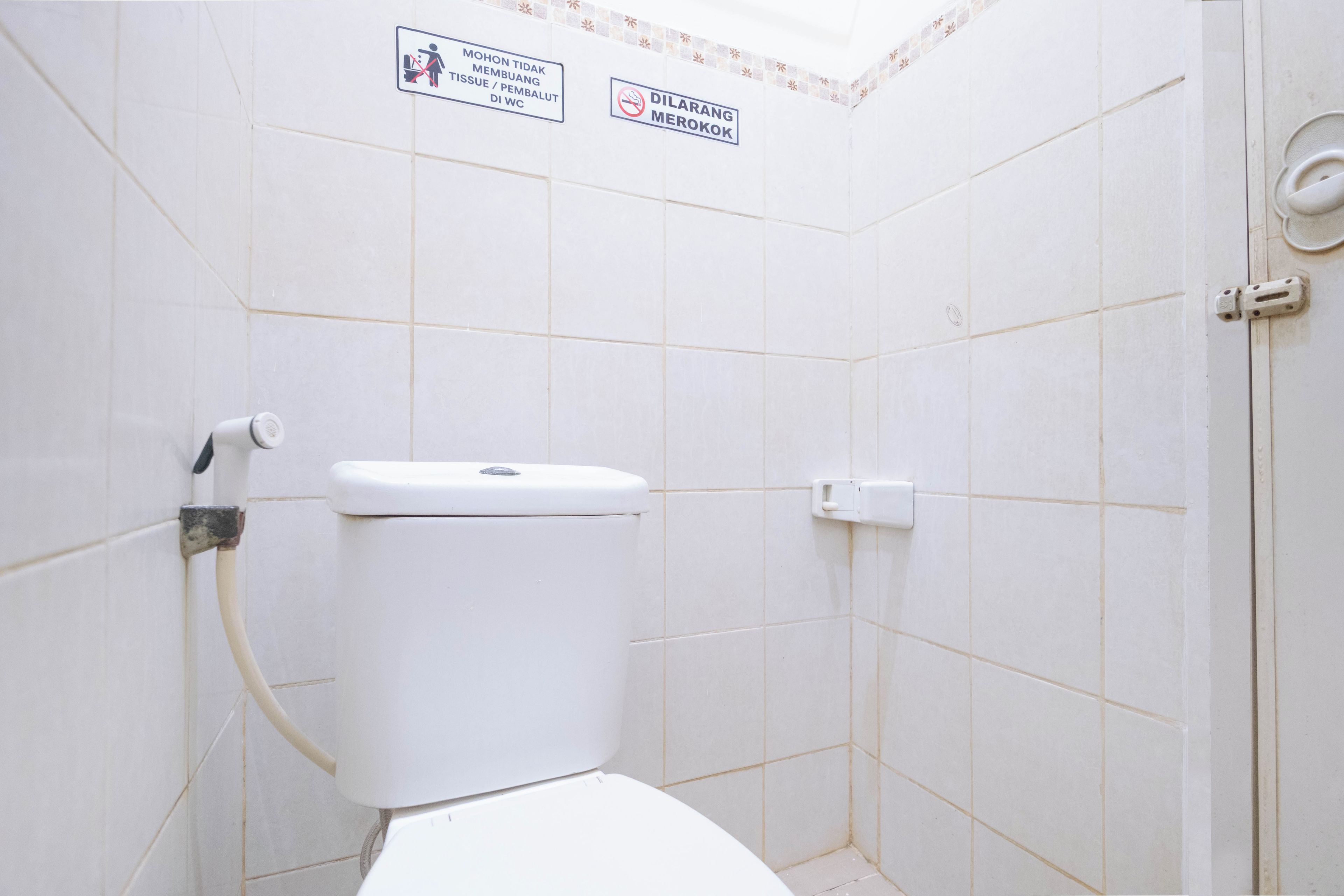 A small, white-tiled bathroom with a toilet, a hand dryer, and two signs indicating no tissue or paper towels in the toilet and no smoking.
