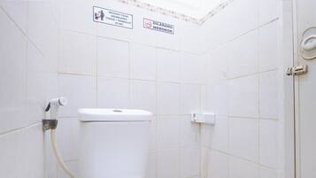 A small, white-tiled bathroom with a toilet, a hand dryer, and two signs indicating no tissue or paper towels in the toilet and no smoking.