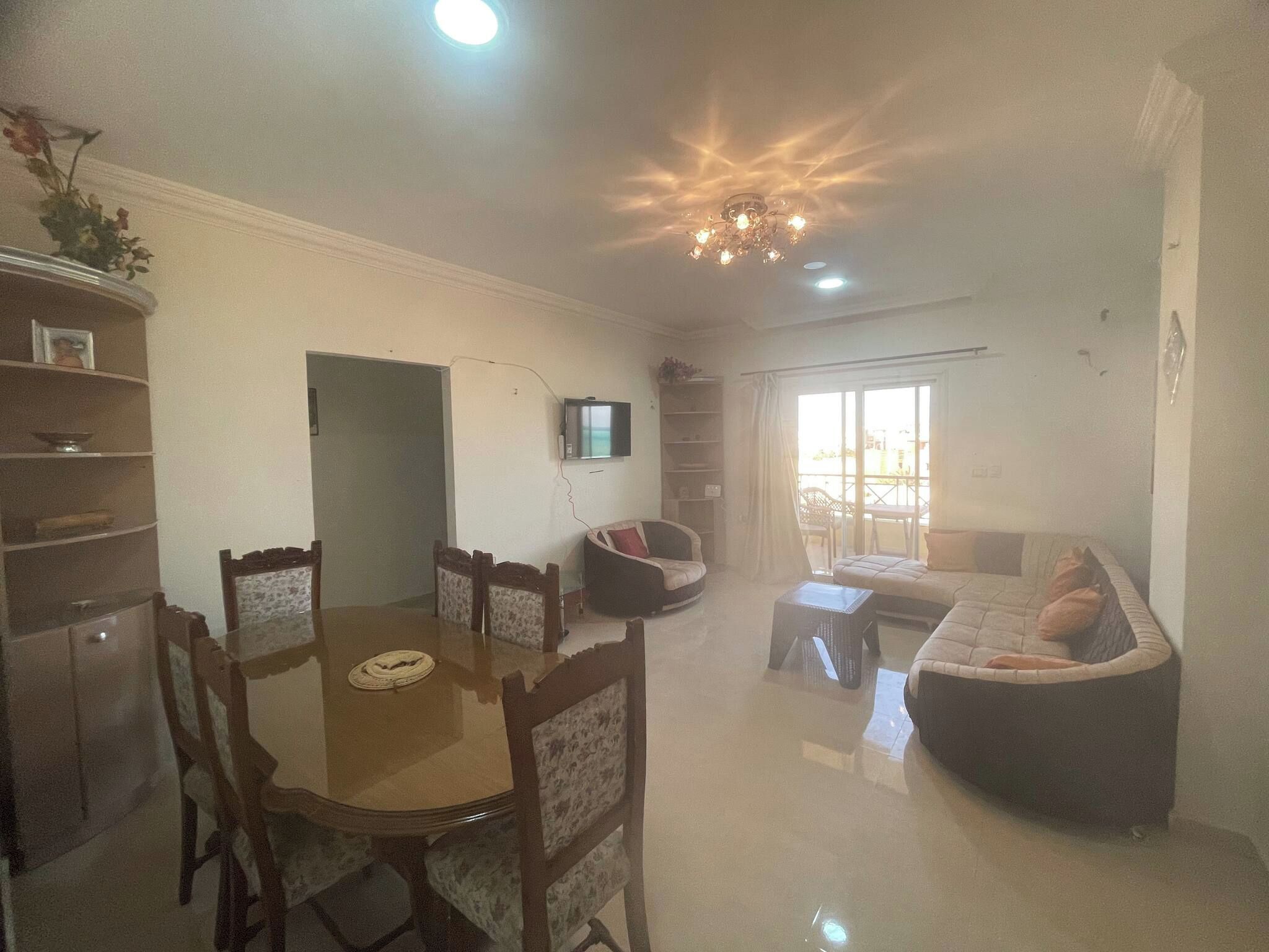 A dining area with a table and chairs, a television mounted on the wall, and a sofa in the living room.