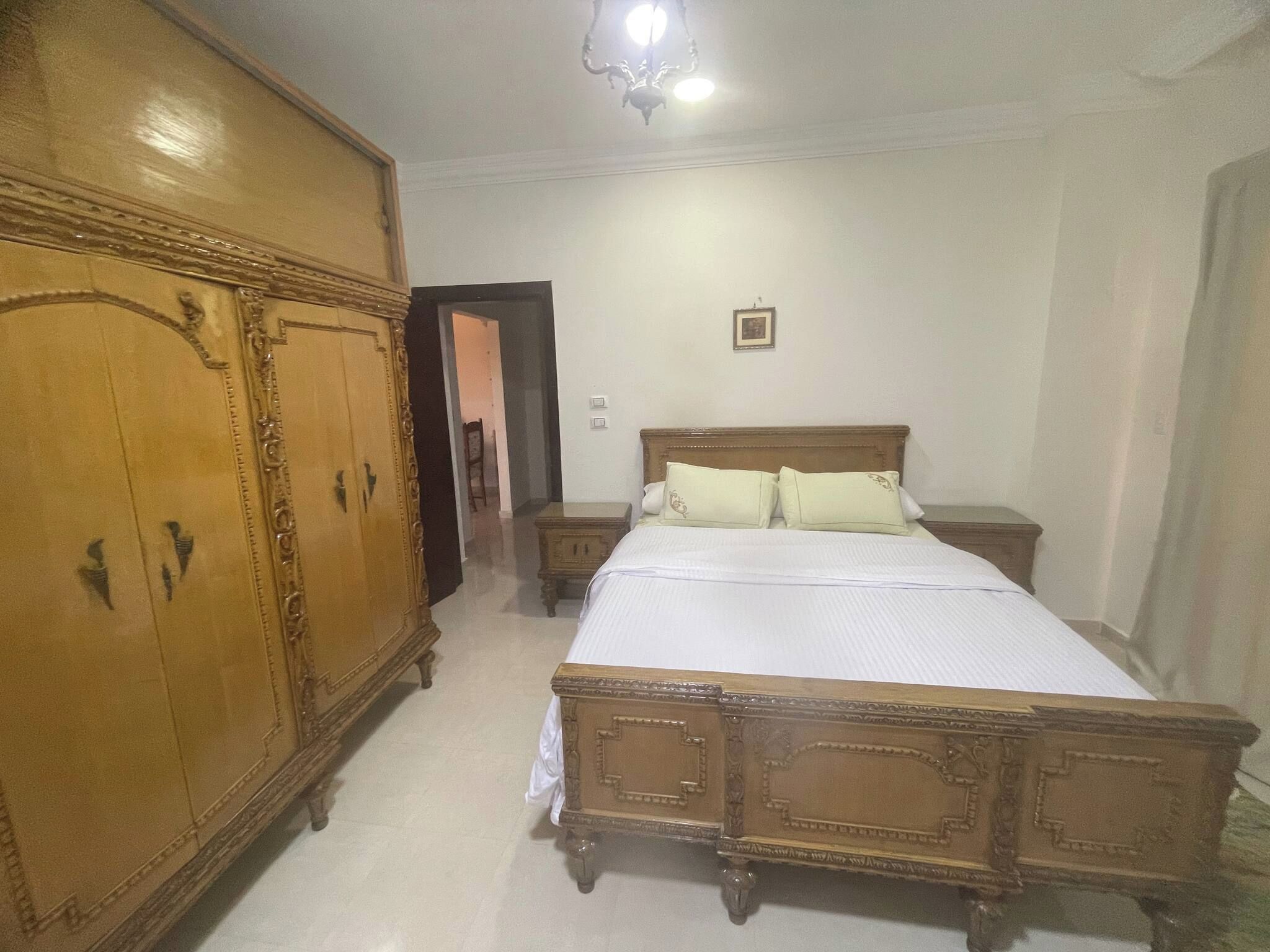 A bedroom with a large wooden wardrobe, a bed with a wooden frame, and a nightstand.