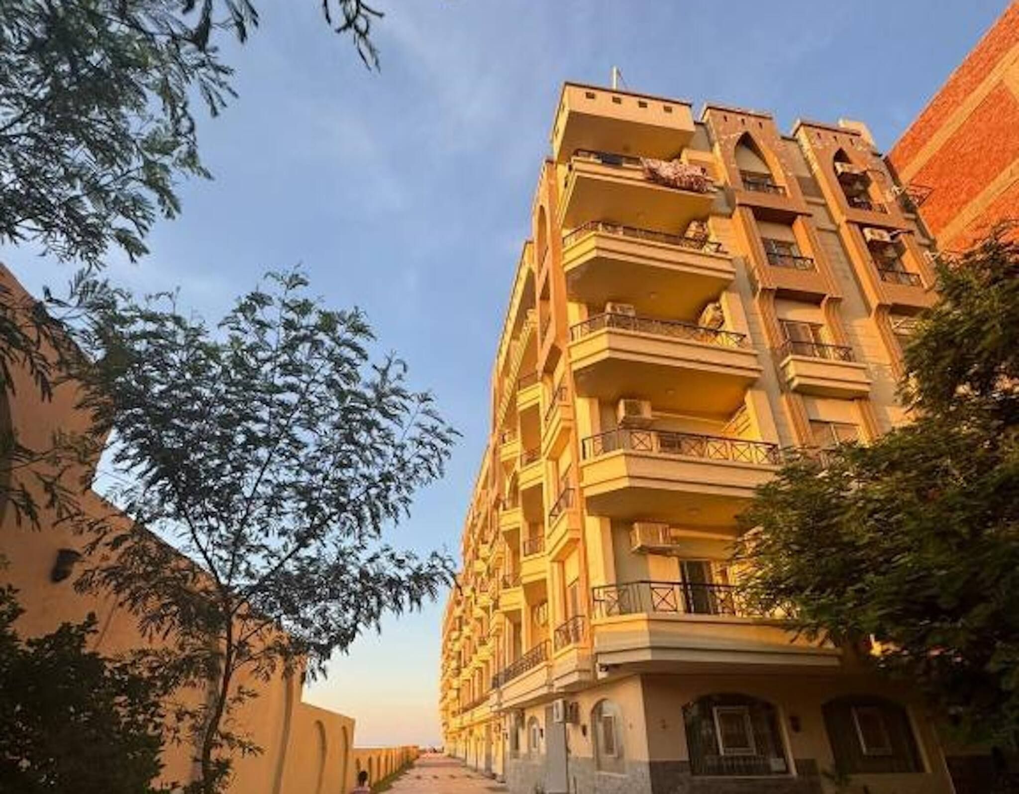 A multi-story building with balconies, a clear sky, and trees.