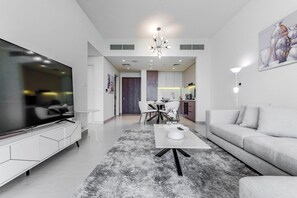 A modern living room with a flat-screen TV, a white sofa, a coffee table, and a dining area with chairs and a table. - HAVN - 1 Bed in Vista Prestige, Dubai Sports City (Dubai)