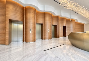 A modern lobby with a marble floor, wooden paneling, and a reception desk. - HAVN - 1 Bed in Vista Prestige, Dubai Sports City (Dubai)