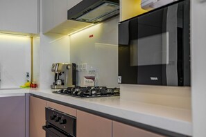 A modern kitchen with a gas stove, coffee maker, and a refrigerator. - HAVN - 1 Bed in Vista Prestige, Dubai Sports City (Dubai)