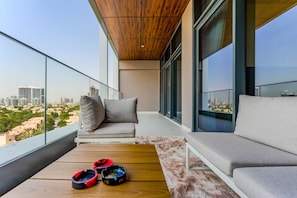 A balcony with a sofa and cushions, a wooden table, and a pair of shoes. - HAVN - 1 Bed in Vista Prestige, Dubai Sports City (Dubai)