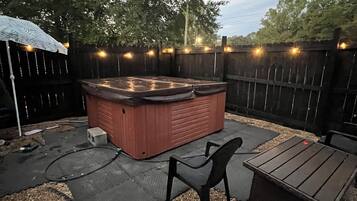 A backyard with a hot tub, a wooden deck, and a seating area.