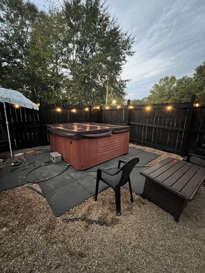 A backyard with a hot tub, a wooden deck, and a seating area.