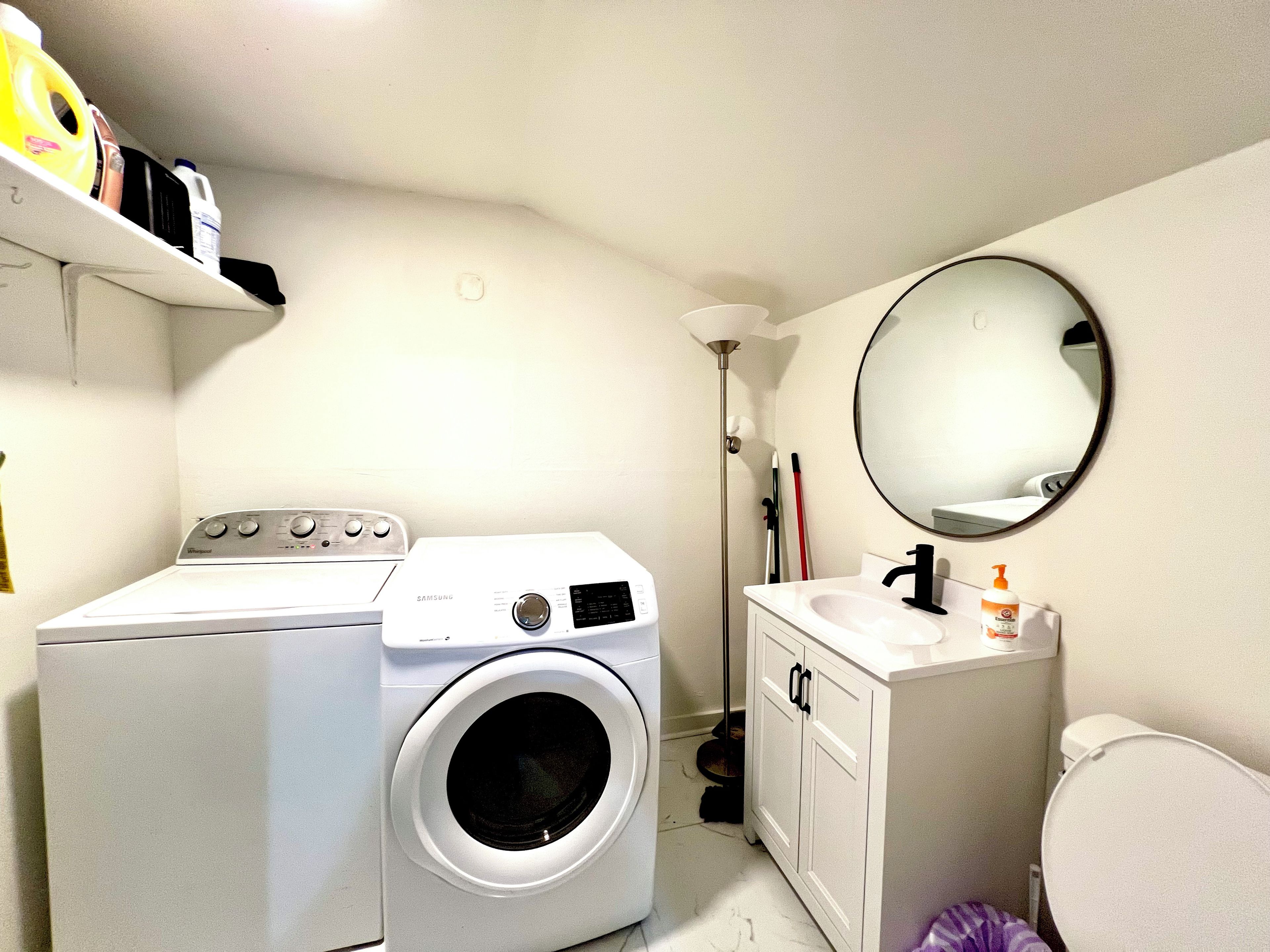 A compact laundry room with a washing machine, a sink, and a mirror.