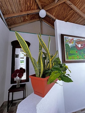 A room with a wooden ceiling, a potted plant, a framed painting, and a small table with a vase of flowers. - La Casa del Banquete (San Andrés)
