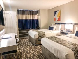 A hotel room with a bed, a desk, a chair, a TV, and a window with curtains.