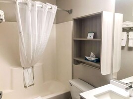 A bathroom with a shower curtain, a toilet, a sink, and a shelf with a tissue box.