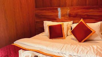 Habitación de hotel con cabecera de madera, cama con ropa blanca y almohadas rojas, y dos controles remotos sobre una toalla.