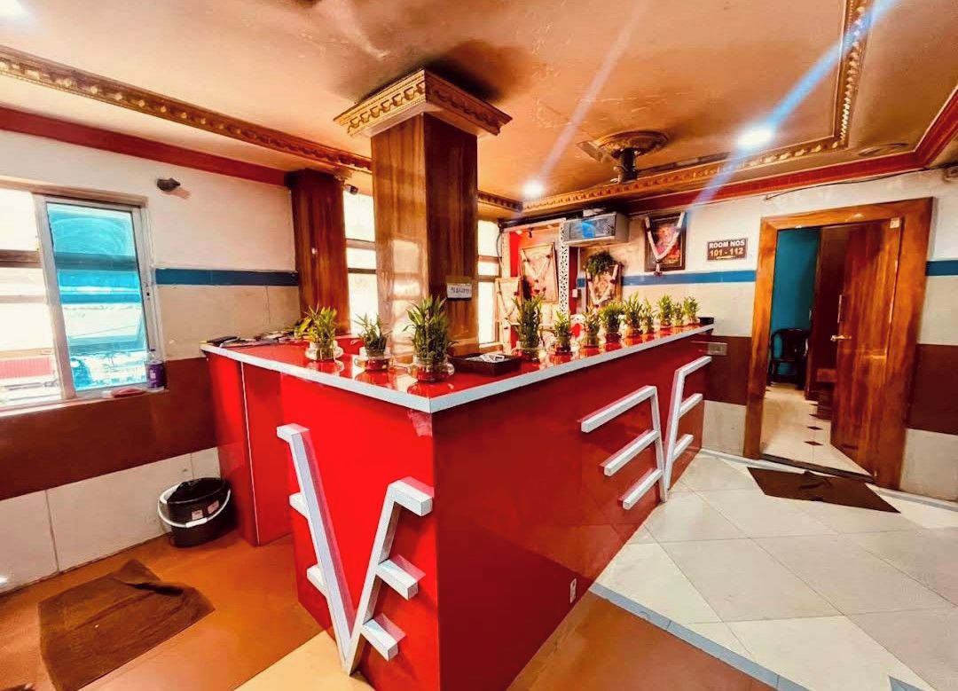 A hotel lobby with a red reception desk, a large window, and a sign indicating room numbers.