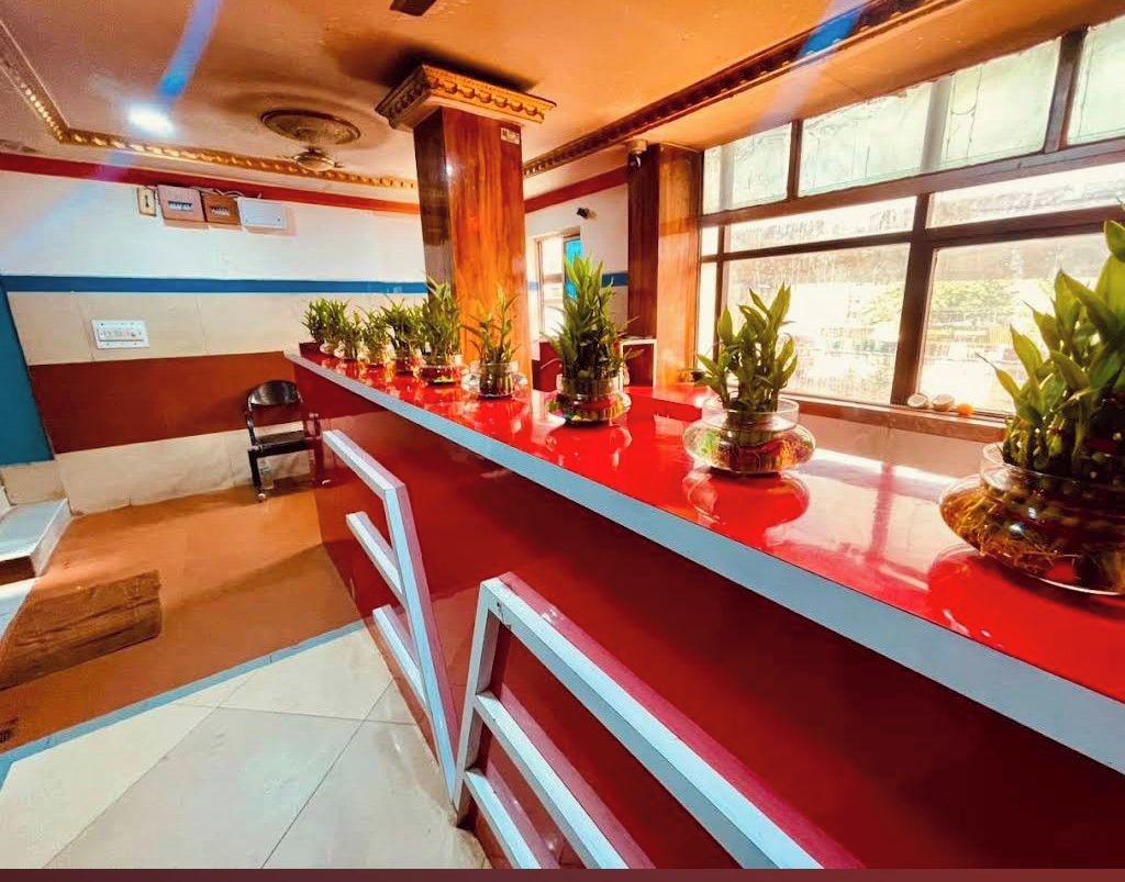 Un área de recepción con mostrador rojo, plantas en macetas, una silla y ventana con vistas.