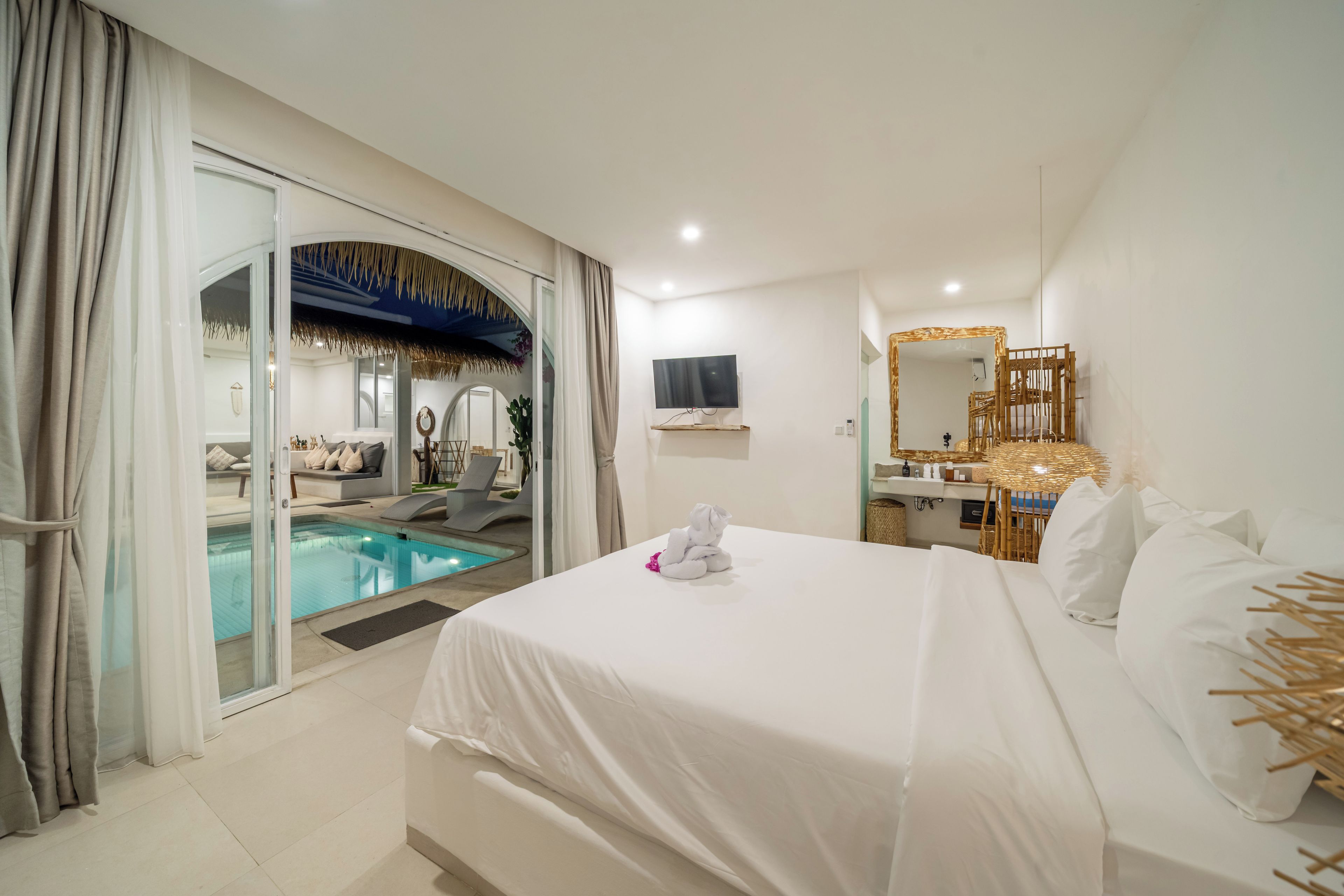 Habitación de hotel con cama, televisión, baño con espejo y zona de piscina.