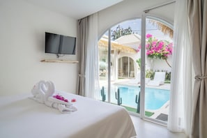 A hotel room with a bed, a television, and a view of an outdoor swimming pool. - Beverly Villa (Kuta Selatan)