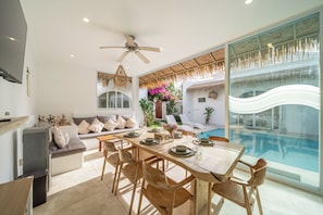 Un comedor moderno con vista a la piscina, un ventilador de techo y una zona de estar con cojines.
