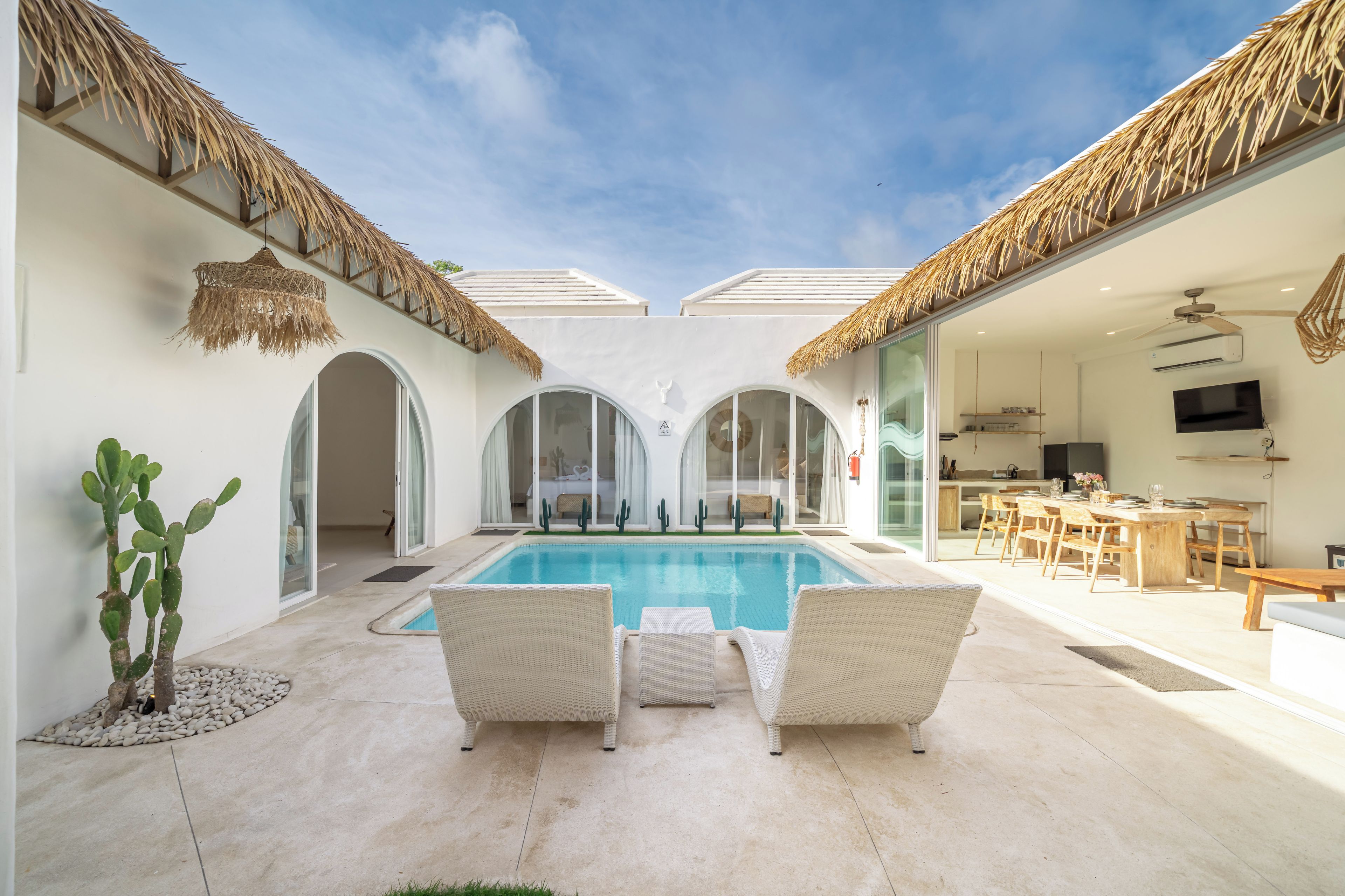 Un área de piscina con sillones reclinables, una cocina con mesa de comedor y una planta de cactus.