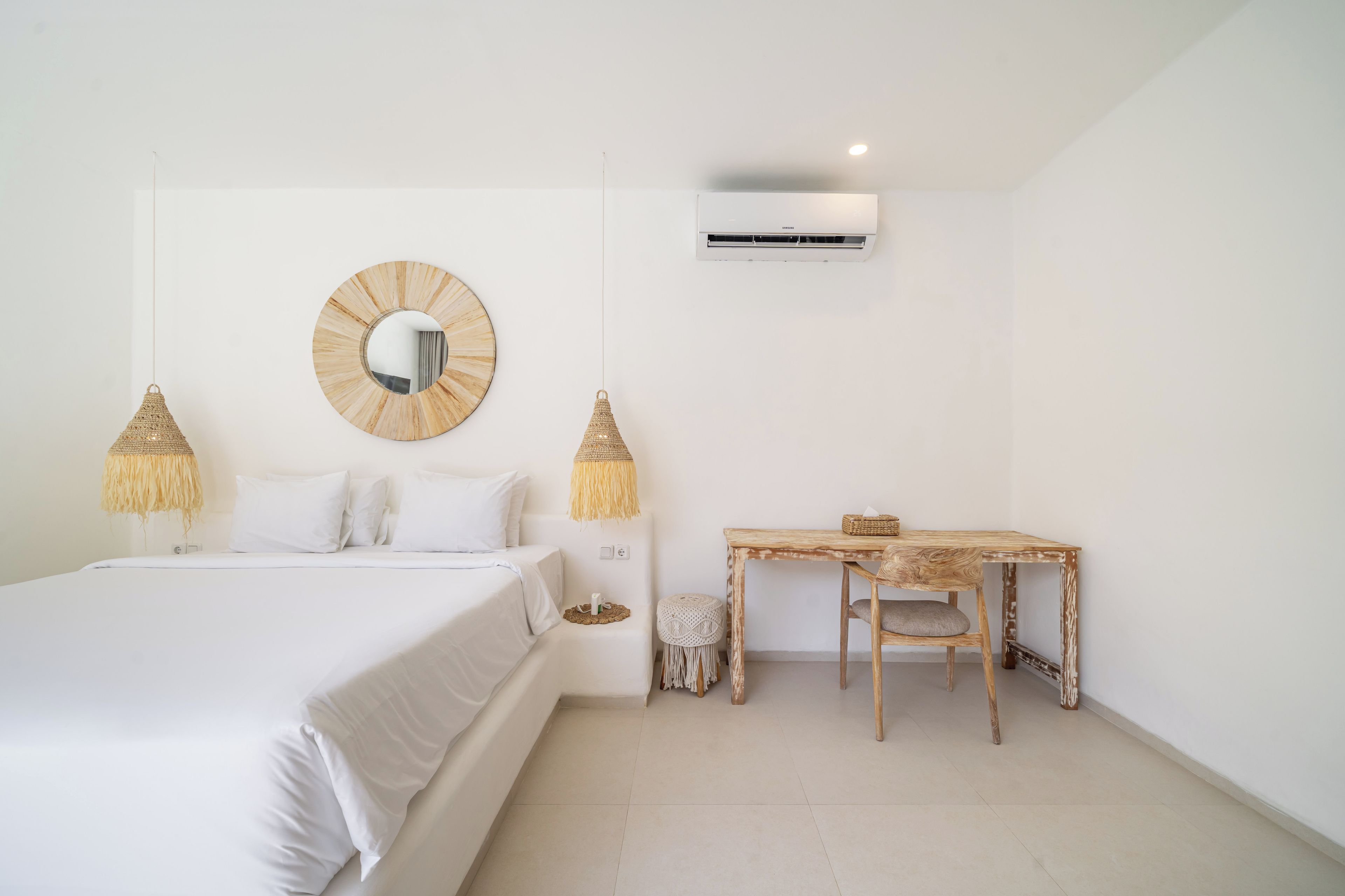 A bedroom with a bed, a round mirror, two hanging lamps, a desk, and an air conditioning unit.