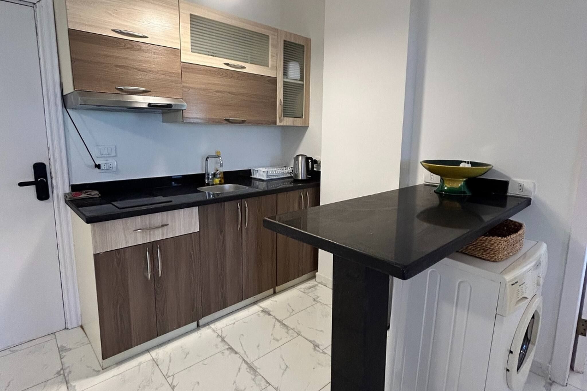 Een functionele keuken met een ingebouwde wasmachine, een spoelbak en houten keukenkastjes.
