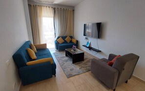 Un salon avec un canapé bleu, un fauteuil gris, une table basse et un téléviseur à écran plat fixé au mur.