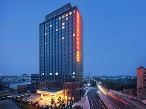 A high-rise building with a modern glass facade, a prominent entrance with a canopy, and a busy street with light trails indicating traffic. - Vienna International Hotel (Hangzhou)