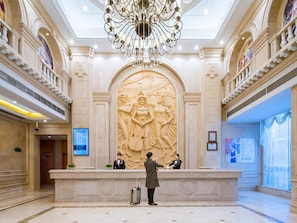 A lobby with a reception desk, a large chandelier, and a detailed wall sculpture. - Vienna International Hotel (Hangzhou)