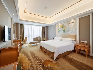 A hotel room with a bed, a desk, a chair, a TV, and a large window with curtains. - Vienna International Hotel (Hangzhou)